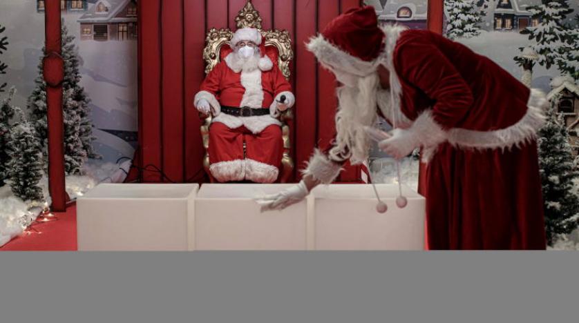 يقوم أحد المساعدين بتطهير مقاعد عدة قبل أن يأتي الأطفال الآخرون للقاء «بابا نويل» الذي يرتدي قناعاً للوجه بمركز تجاري في فالنسيا شرق إسبانيا (إ.ب.أ)