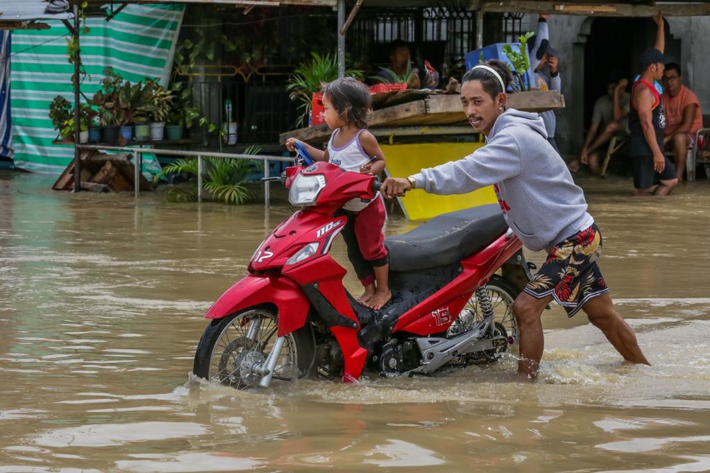 رجل يدفع درجة نارية على متنها طفل عبر طريق تغمره المياه في محافظة بولاكان بالفلبين يوم 26 سبتمبر 2022. (شينخوا)