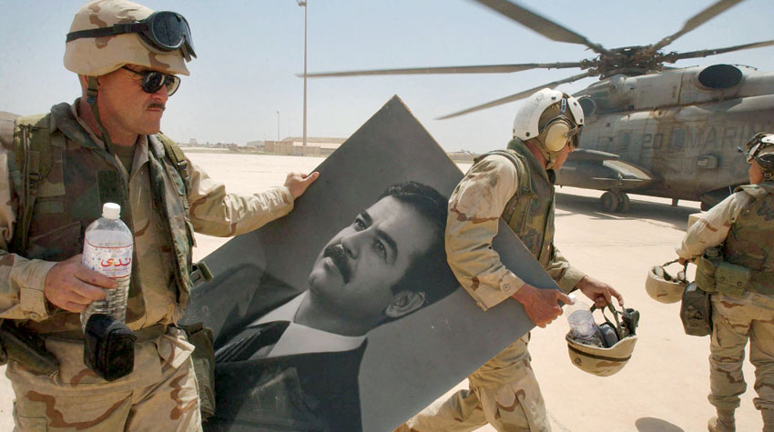 جنود أميركيون في مطار بغداد مع صورة لصدام حسين بعد إطاحة نظامه يوم 14 أبريل 2003 (أ.ف.ب)