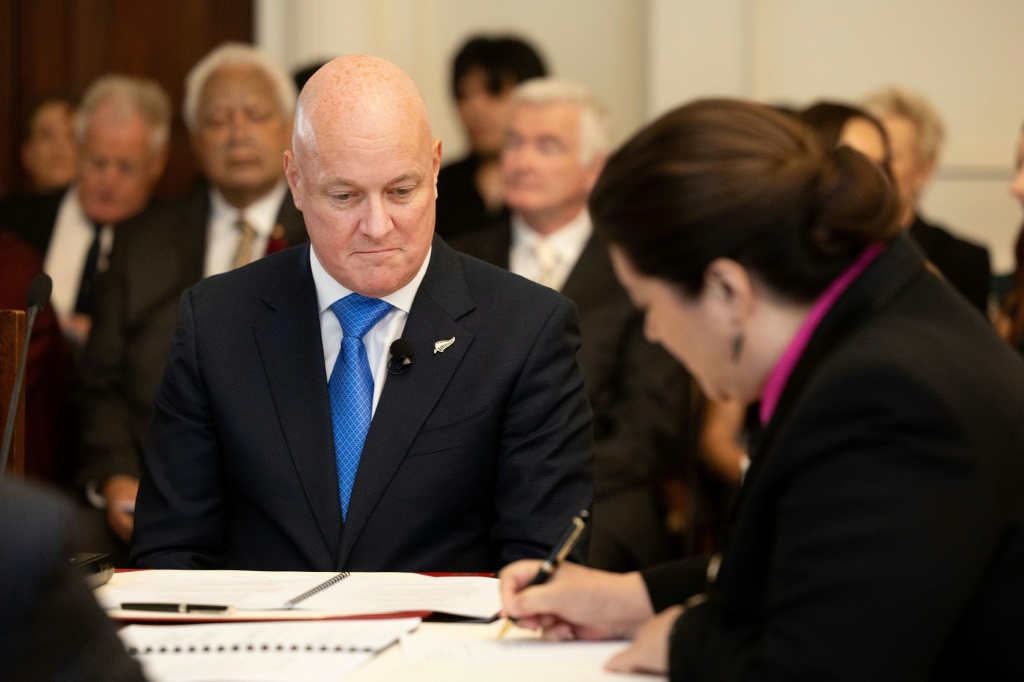 كريستوفر لوكسون (يسار) ينظر بينما الحاكم العام السيدة سيندي كيرو يوقع الوثائق التي جعلته رئيسًا لوزراء نيوزيلندا رسميًا يوم الاثنين (ا ف ب)