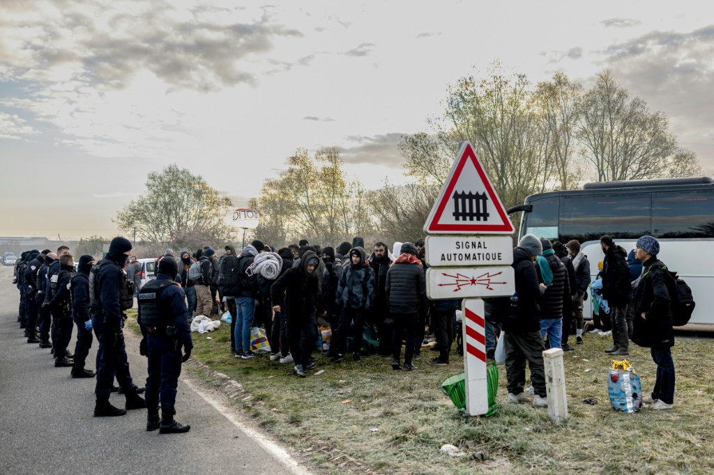 مهاجرون محاطون بعناصر من الشرطة الفرنسية ينتظرون نقلهم الى مراكز استقبال في لون بلاج بشمال فرنسا في 30 تشرين الثاني/نوفمبر 2023. (أ ف ب)   