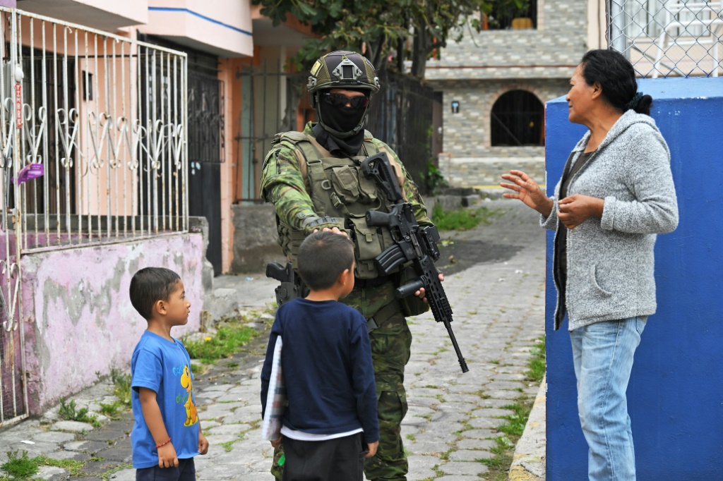 جندي يتحدث إلى سيدة وطفلين في حي موران في العاصمة الاكوادورية كيتو في 11 كانون الثاني/يناير 2024 (ا ف ب)