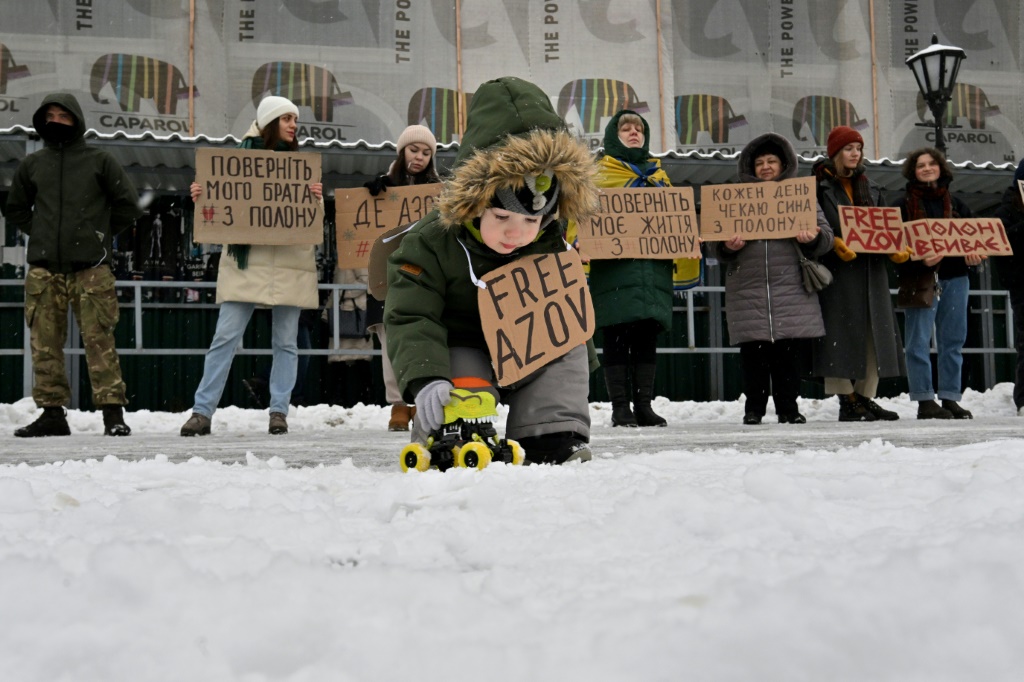 طفل مع اقرباء سجناء حرب اوكرانيين من وحدة آزوف يحملون لافتات تدعو الى مبادلتهم بسجناء روس، خلال تجمع في كييف في 21 كانون الثاني/يناير 2024. (أ ف ب)   