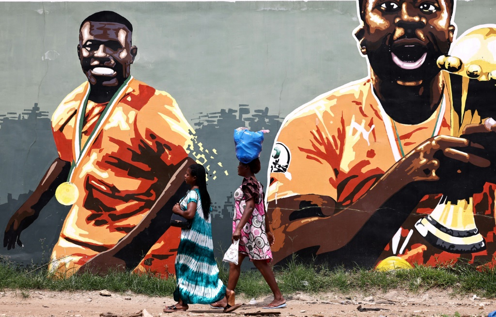 نساء يمرنّ مقابل جداية لنجوم ساحل العاج المتوجين بكأس أمم إفريقيا 2015 في أبيدجان في 20 كانون الثاني/يناير 2024 خلال كأس أمم إفريقيا (ا ف ب)