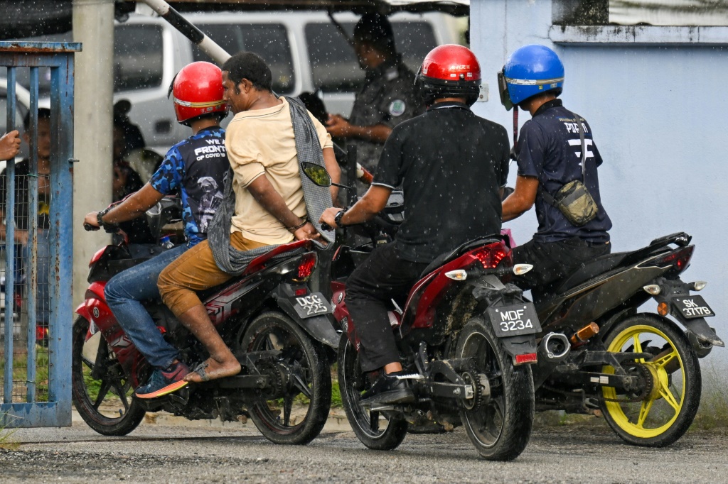 السلطات الماليزية ترافق معتقلاً مكبل اليدين بعد فرار أكثر من 100 لاجئ من الروهينجا من مركز احتجاز في ولاية بيراك الشمالية (أ ف ب)   