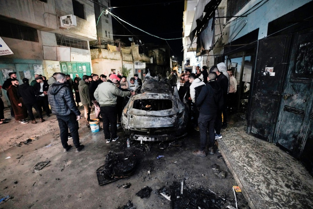 أشخاص يتفقدون سيارة في جنين في 22 شباط/فبراير 2024 قتل فيها فلسطيني وجرح أربعة في ضربة إسرائيلية على سيارة في مخيم جنين للاجئين في الضفة الغربية المحتلة (ا ف ب)