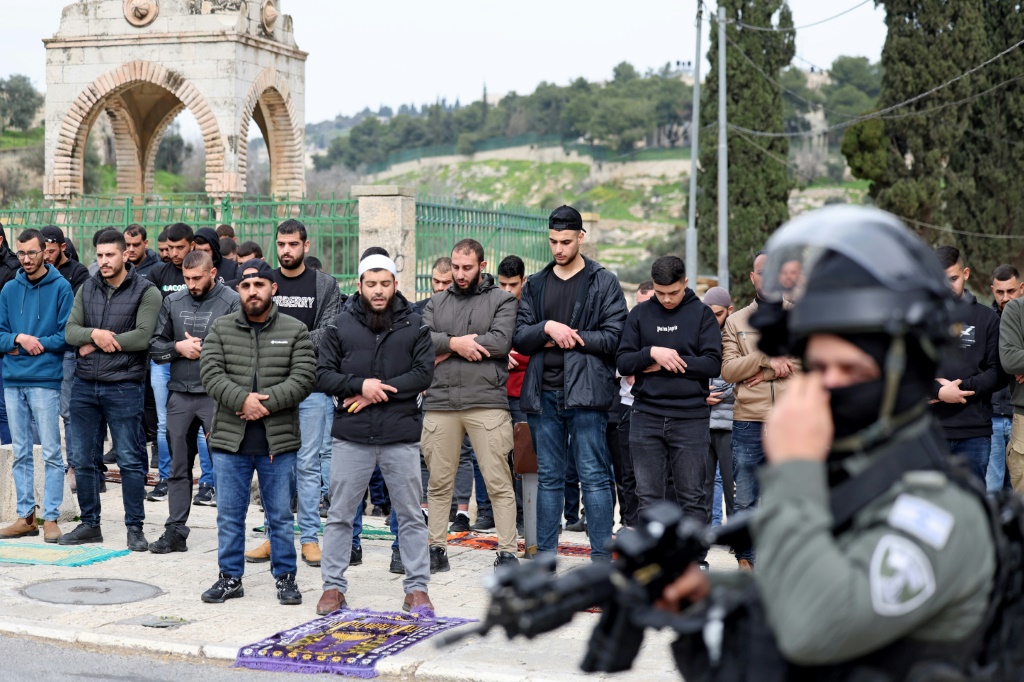 عنصر أمن إسرائيلي يقف بينما يؤدي مسلمون فلسطينيون صلا الجمعة في أحد شوارع القدس الشرقية في 23 شباط/فبراير 2024 (ا ف ب)