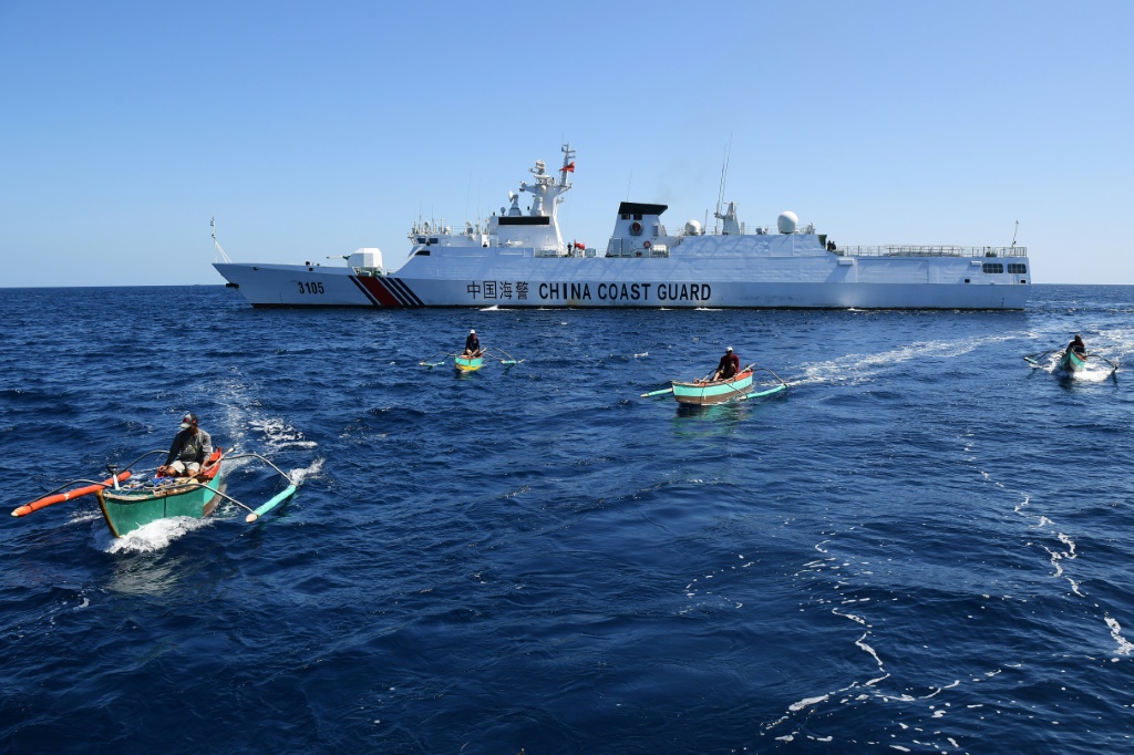 صيادون فلبينيون يبحرون أمام سفينة تابعة لخفر السواحل الصيني بالقرب من منطقة سكاربورو شول، التي كانت نقطة اشتعال بين البلدين منذ استولت عليها الصين من الفلبين في عام 2012 (ا ف ب)