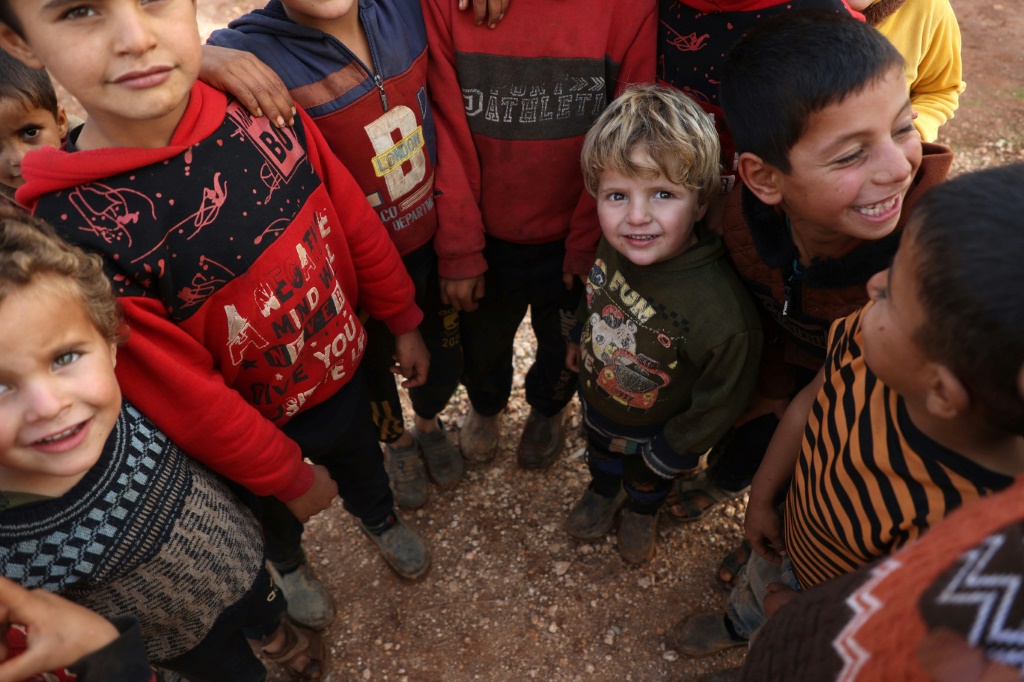 أطفال سوريون ينتظرون الحصول على مساعدات يوزعها برنامج الأغذية العالمي التابع للأمم المتحدة على نازحين في مخيّم بضواحي مدينة إدلب في شمال غرب سوريا في السادس من كانون الأول/ديسمبر 2023 (أ ف ب)   