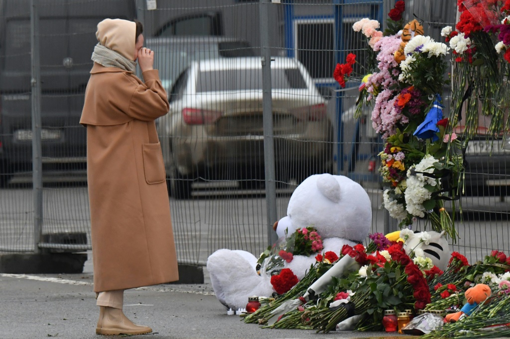    صورة مؤرخة في 23 آذار/مارس 2024 لامرأة أمام نصب تذكاري في موقه الهجوم على صالة كروكوس سيتي هول في ضاحية موسكو (أ ف ب)   