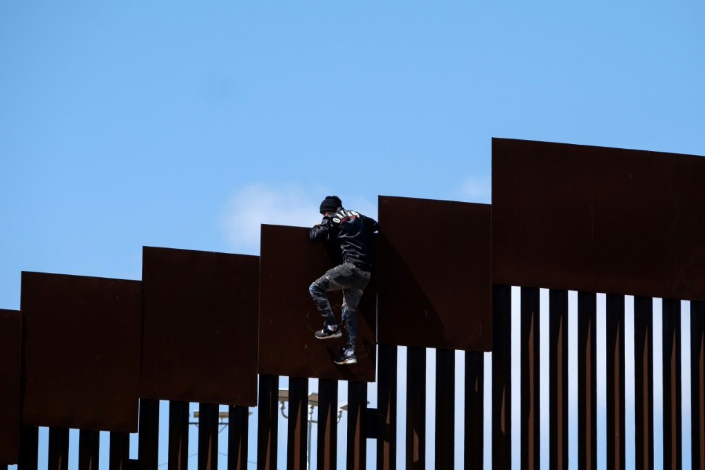 مهاجر يتسلق السياج الحدودي قرب تيخوانا بالمكسيك لدخول الولايات المتحدة في أيار مايو 2023 (ا ف ب)