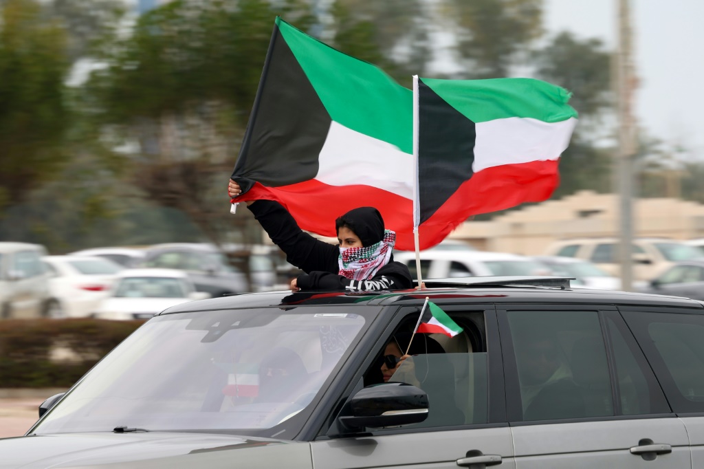 طفل يلوّح بعلم الكويت من داخل سيارة خلال الاحتفال باليوم الوطني الثالث والستين في العاصمة الكويتية، في 25 شباط/فبراير 2024 (ا ف ب)