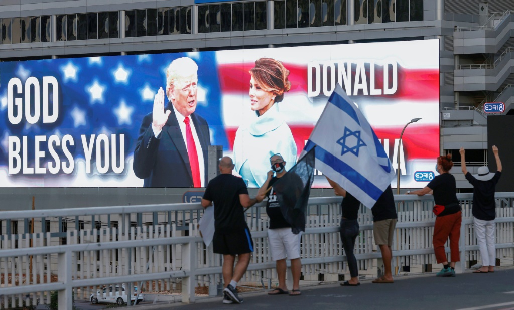 متظاهرون مناهضون للحكومة الإسرائيلية يرفعون العلم الإسرائيلي على جسر أمامه صورة كبيرة لدونالد ترامب وزوجته ميلانيا في تل أبيب بتاريخ 3 تشرين الأول/أكتوبر 2020 (ا ف ب)