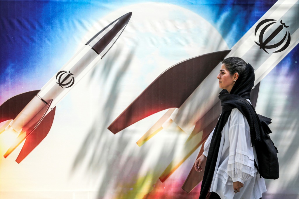    امرأة تمر أمام لافتة عليها صواريخ تحمل شعار جمهورية إيران الإسلامية في وسط طهران (أ ف ب)   