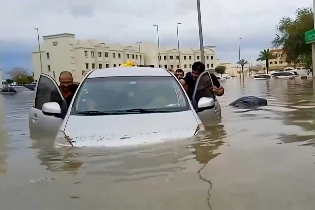 سكان يدفعون سيارة غارقة بالمياه في شارع غمرته المياه في مدينة دبي الصحراوية بعد أن أصابت الأمطار الغزيرة المركز المالي والترفيهي في الخليج بالشلل (ا ف ب)