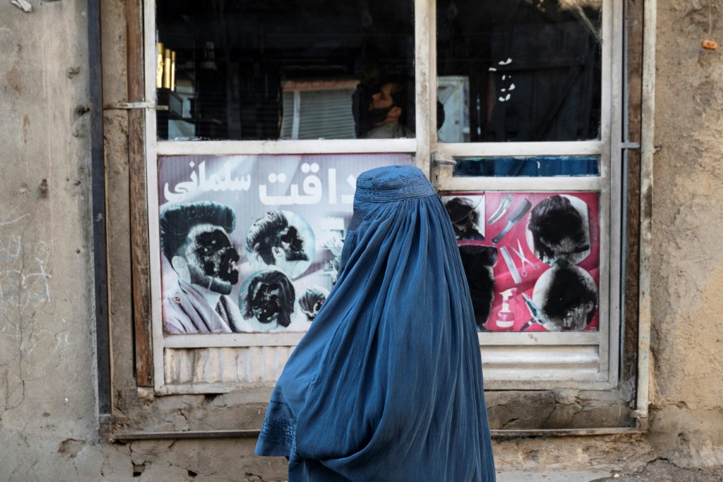 امرأة أفغانية ترتدي البرقع تمر أمام محل حلاقة في كابول في 31 كانون الثاني/يناير 2024 (ا ف ب)   